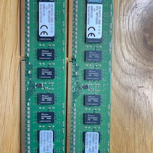 May include: Two green computer memory modules with black labels. The labels include the text "SK hynix Kingston 8GB 2Rx8 PC3-10600E-9-13-E3 KTA-MP1333/8G 1.5V BSMH1811501 Warranty Void Removed CE 9965525-140 ADOLF 0000006850771-5000502 BMJP7-195CKV-4V9KT ASSY IN CHINA (1)"