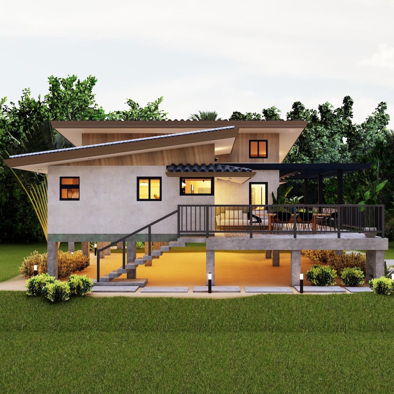 Op de afbeelding: Een modern, eenlaags huis met een lichtgrijze buitenkant en een houten dak. Het huis heeft grote ramen en een overdekt terras met een railing. Het huis is gebouwd op palen en heeft een trap die naar het terras leidt.
