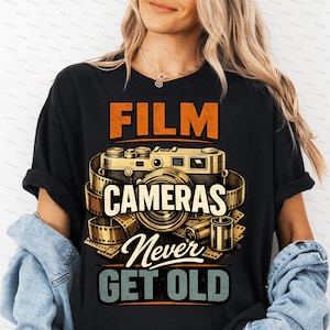 Op de afbeelding: Zwart T-shirt met een vintage camera-ontwerp en de tekst "FILM CAMERAS Never GET OLD" in oranje, wit en blauw. Het ontwerp bevat een filmcamera, filmstrips en filmcassettes. Het shirt is gemaakt van een zacht materiaal.
