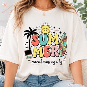 Peut inclure: T-shirt crème avec un motif coloré "SUMMER", représentant un soleil souriant, un palmier et une planche de surf. Le design comprend le texte "remembering my why". Le t-shirt est de coupe décontractée.