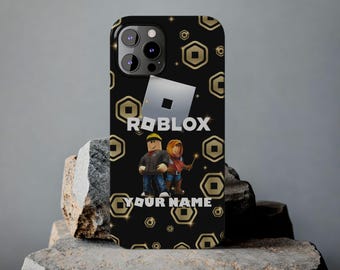 Könnte beinhalten: Eine schwarze Smartphone-Hülle mit einem sich wiederholenden goldenen Sechseckmuster, dem weißen Roblox-Logo und zwei Zeichentrickfiguren. Unter den Figuren steht der Text YOUR NAME in weißen Großbuchstaben auf dunklem Grund.