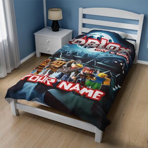 May include: A black and blue twin-sized fleece blanket with a Roblox Day & Night design. The blanket features a group of Roblox characters in a forest setting. The text "Your Name" is printed on the blanket.