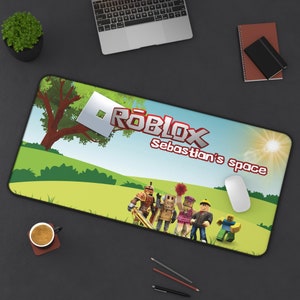 Könnte beinhalten: Eine rechteckige Schreibtischunterlage mit Roblox-Motiv, die eine grüne Landschaft, einen Baum und fünf blockartige Figuren zeigt. Das Design enthält das Roblox-Logo und den Text "Sebastian's space" in roter Schrift vor einem hellen Himmel.