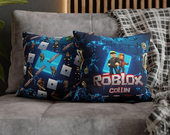 May include: Two square throw pillows featuring a dark blue background with a digital pattern. One pillow displays a repeating Roblox logo and character print. The other features a large Roblox logo, the name COLLIN, and two character figures.