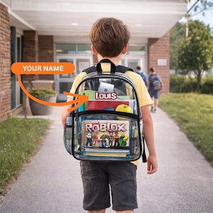 May include: A transparent backpack with black edging, packed with school items like notebooks and a book featuring "ROBLOX". The backpack has a mesh side pocket. The name "LOUIS" is displayed on a label inside.
