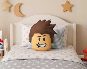 May include: A plush throw pillow shaped like a stylized character head with brown spiky hair, a tan complexion, and a wide grin featuring a sparkling tooth. The character wears colorful headphones over the ears, with a smooth, soft fabric finish.