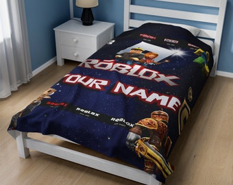 Peut inclure: Une couverture bleu foncé avec un fond sur le thème de l'espace, des graphismes de personnages Roblox, le logo Roblox et le texte "YOUR NAME" en grandes lettres blanches. Le design inclut des bandes noires avec le logo et des années.
