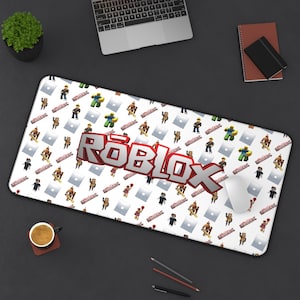 May include: A rectangular white mousepad featuring a pattern of Roblox characters and logos. The large, 3D Roblox logo is in red and white. A computer mouse rests on the pad, with a laptop, coffee cup, and notepad in the background.