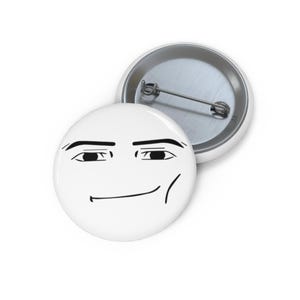 Könnte beinhalten: Ein runder Ansteckbutton mit weißem Hintergrund und einer schwarzen Strichzeichnung eines grinsenden Gesichts. Das Design zeigt dicke Augenbrauen, schmale Augen und ein dezentes, einseitiges Lächeln. Die Rückseite hat eine silberne Metallnadel.