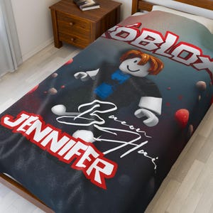 May include: A twin-size bedspread featuring a Roblox character design. The design includes the Roblox logo in red and white, a cartoon character, and the name "Jennifer" in red. The background is dark with red and white accents.