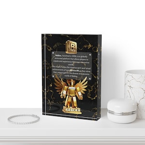 Może przedstawiać: Czarna i złota akrylowa tabliczka z złotym logo Roblox i złotą figurką Roblox z skrzydłami. Tabliczka ma marmurowy wzór i tekst "Roblox, uruchomiony w 2006 roku, to globalnie znana platforma, która pozwala graczom tworzyć i doświadczać własnych interaktywnych światów. Ta trofea honoruje kreatywnego ducha i wirtualne osiągnięcia użytkowników, gdy wytyczają swoją unikalną ścieżkę w zróżnicowanym i dynamicznym świecie Roblox."