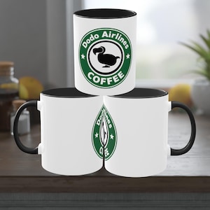 Può includere: Tazze da caffè in ceramica bianca con interni e manici neri. Ogni tazza presenta un logo verde e bianco con la scritta "Dodo Airlines Coffee" e un'illustrazione di un dodo. Le tazze sono impilate su una superficie di legno.