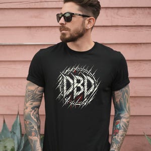 May include: Black t-shirt with the white text "DBD" in a stylized, distressed font, surrounded by a circular design of white lines. The shirt has short sleeves.
