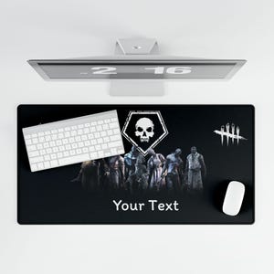 May include: Black rectangular desk mat featuring a skull and character graphic. A white keyboard and mouse are on the mat. The text "Your Text" is printed on the mat.