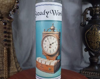 May include: A teal blue candle with a green base. The candle has a white label with the text "Steady Work" and an image of an antique clock with a wooden case and a brass face.