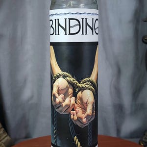 May include: A white candle with a black and white image of bound hands and the word "BINDING" printed on the front.