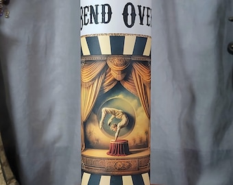 May include: A glass candle with a purple wax base and a white label that says "Bend Over". The label also features a vintage illustration of a person performing a contortionist act on a stage.