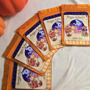 May include: A collection of orange foil pouches, each with a Halloween sticker. The sticker design includes a cartoon ghost, a coffee cup, and the text "Fwoggo Falloween" and "Sticker Bag". An orange pumpkin is visible in the background.