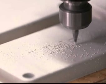 Puede incluir: Primer plano de un objeto rectangular blanco que se está grabando con la palabra "NEXT" con una pequeña broca.