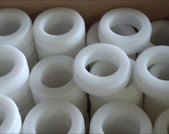 Puede incluir: Una caja llena de anillos de plástico blanco. Los anillos están apilados uno encima del otro y todos son del mismo tamaño.