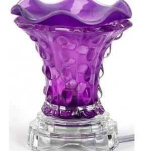 Könnte beinhalten: Lilafarbener Glas-Duftöldiffusor mit strukturiertem Design und einem klaren Glasfuß. Der Diffusor hat eine gewellte Oberseite und eine Glühbirne im Inneren.