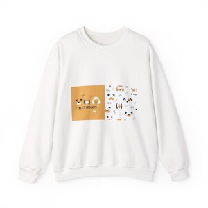 Pode incluir: Camisola branca com um design de cães. O design apresenta rostos de cães de desenho animado e o texto "BEST FRIENDS" em um quadrado marrom. O outro lado da camisola tem mais rostos de cães em um fundo branco.