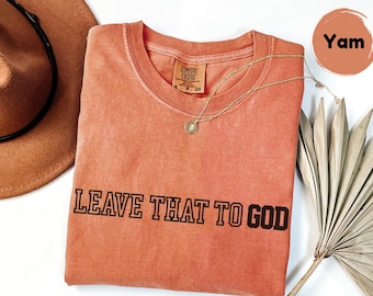 May include: A coral colored t-shirt with the text "LEAVE THAT TO GOD" printed in black. The shirt is made of a soft, comfortable material.