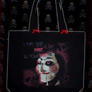 May include: Black tote bag with the text "I PUT THE HOT IN PSYCHOTIC" and a graphic of a character with a spiral design on the cheek. The bag has black handles and small red bows at the top.