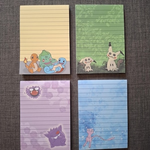 Könnte beinhalten: Vier linierte Notizblöcke mit farbenfrohen Pokémon-Charakterillustrationen. Die Notizblöcke haben einen gelben, grünen, lila und blauen Hintergrund. Jeder Notizblock hat ein anderes Pokémon-Design, darunter Glumanda, Bisasam, Schiggy, Mimigma, Gengar, Nebulak und Mew.