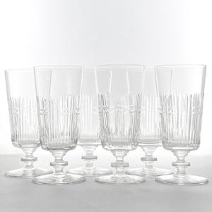 May include: A set of six clear, stemmed champagne flutes. Each glass features vertical etched lines and a decorative band near the top. The glasses have a classic, elegant design, perfect for special occasions.