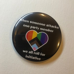 May include: A black button with a rainbow heart and the text "When someone attacks one party member we all roll for initiative".