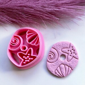 May include: Pink plastic cookie cutters and a pink clay imprint of seashells, starfish, and swirls.