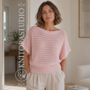Op de afbeelding: Een lichtroze gebreide trui met korte mouwen, een brede boothals en een geribbelde zoom. Het kledingstuk heeft een gestructureerd patroon met open steken over het hele lijf. De tekst KNITORSTUDIO staat verticaal aan de linkerkant van de afbeelding.