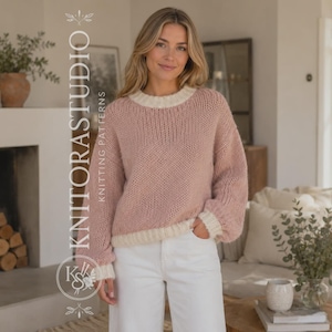 Puede incluir: Un suéter de punto grueso en un suave color rosa empolvado con cuello redondo, puños y dobladillo de color crema. El suéter tiene mangas largas y un corte relajado, combinado con pantalones blancos. El texto KNITORASTUDIO KNITTING PATTERNS es visible.