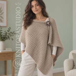 Peut inclure: Un poncho tricoté beige présentant une texture côtelée en diagonale et une section en maille unie. Le vêtement est fixé à l'épaule par un bouton marron foncé en forme de fleur. Le texte KNITORASTUDIO est visible verticalement sur la gauche.