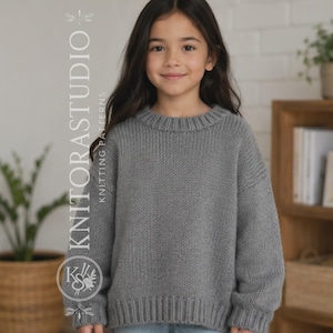 Op de afbeelding: Een grijze gebreide trui met lange mouwen, een geribbelde ronde hals en geribbelde boorden. De trui heeft een grove breistructuur en een relaxte pasvorm. De tekst KNITORASTUDIO KNITTING PATTERNS is zichtbaar aan de linkerkant van de afbeelding.