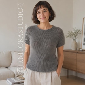 Könnte beinhalten: Ein kurzärmeliger, anthrazitfarbener Strickpullover mit gerippter Textur und Rundhalsausschnitt. Das Kleidungsstück wird mit dem vertikal auf der linken Seite des Bildes sichtbaren Text KNITORASTUDIO KNITTING PATTERNS dargestellt.