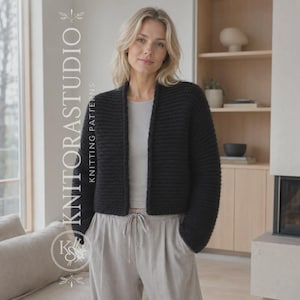 May include: A black, long-sleeved, open-front knit cardigan with a textured stitch pattern. The garment is worn over a light grey top and light grey drawstring trousers. The text KNITORASTUDIO KNITTING PATTERNS is visible on the left side.