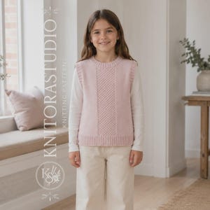 Op de afbeelding: Een lichtroze mouwloze gebreide spencer met een centraal verticaal paneel met textuur, gedragen over een wit shirt met lange mouwen en een lichte broek. De afbeelding bevat de verticale tekst KNITORASTUDIO KNITTING PATTERNS.