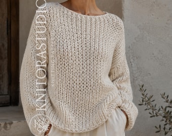Può includere: Un maglione in maglia grossa color bianco sporco con un ampio scollo a barchetta e maniche lunghe e larghe. Il capo presenta una trama a coste verticali su tutta la superficie. Il testo KNITORASTUDIO KNITTING PATTERNS è stampato verticalmente.