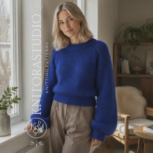 Puede incluir: Un suéter de color azul real vibrante con mangas largas, cuello redondo y puños y dobladillo acanalados. El suéter presenta una textura de punto grueso y se combina con pantalones de color marrón claro. El texto KNITORASTUDIO KNITTING PATTERNS es visible.
