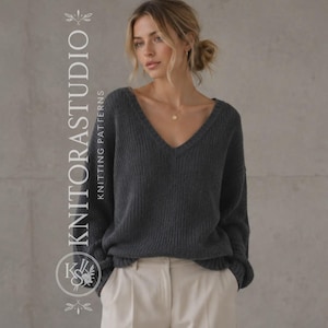 Puede incluir: Un suéter de manga larga en color gris carbón oscuro con un cuello en V profundo y textura de punto acanalado. La prenda se combina con pantalones de color beige claro. El texto KNITORASTUDIO KNITTING PATTERNS y un logo circular son visibles.