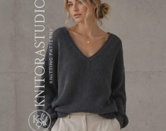 Può includere: Un maglione a maniche lunghe grigio antracite scuro con un profondo scollo a V e una trama a maglia a coste. Il capo è abbinato a pantaloni beige chiaro. Il testo KNITORASTUDIO KNITTING PATTERNS e un logo circolare sono visibili a sinistra.