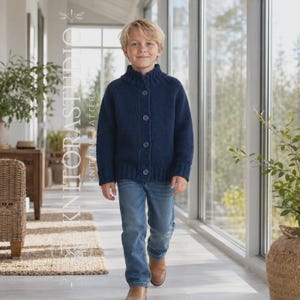 May include: A navy blue long-sleeve knit cardigan with a ribbed mock neck collar and four matching buttons down the front. The garment is paired with blue denim jeans and brown leather shoes, featuring a vertical watermark text KNIT ORA STUDIO.