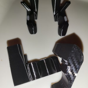 May include: Black 3D-printed components, including two pairs of angled pieces and two upright supports. The parts are arranged on a white surface. The pieces have a glossy finish and appear to be designed for a specific purpose.