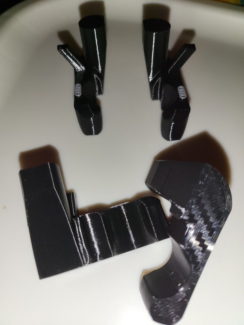 May include: Black 3D-printed components, including two pairs of angled pieces and two upright supports. The parts are arranged on a white surface. The pieces have a glossy finish and appear to be designed for a specific purpose.