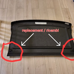 Peut inclure: Une pièce de rechange noire pour panneau de coffre de voiture. Le panneau est rectangulaire avec un bord supérieur légèrement incurvé. Le texte "replacement / ricambi" est écrit sur le panneau. Le panneau a deux clips en plastique de chaque côté.
