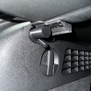 May include: Close-up of a black car interior, featuring an air vent with adjustable directional control and a textured surface. The vent has a circular dial and a series of triangular openings.