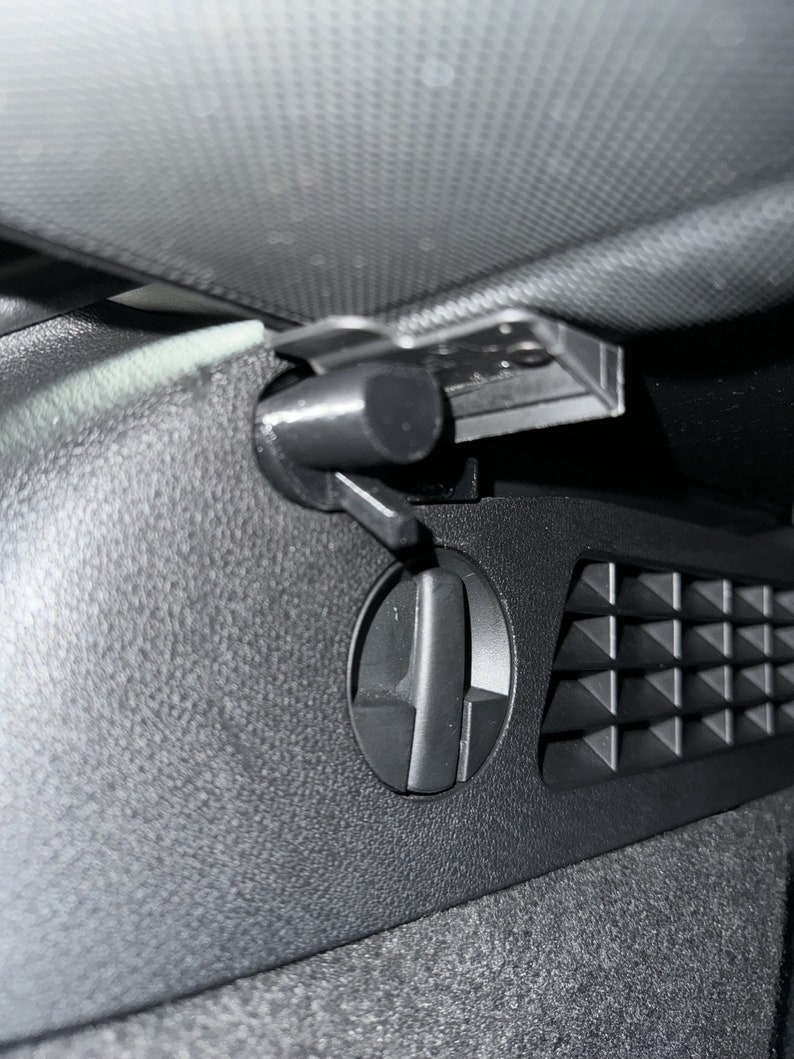 May include: Close-up of a black car interior, featuring an air vent with adjustable directional control and a textured surface. The vent has a circular dial and a series of triangular openings.