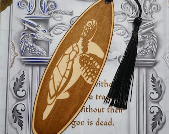 May include: Wooden bookmark shaped like a surfboard with a laser-cut design of a sea turtle. The bookmark has a black tassel.